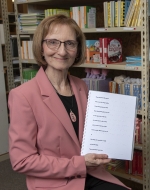 Photo of Debra Bonde in front of bookshelf and holding a Seedlings book