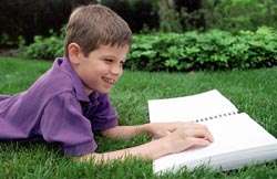Photo of a child reading a braille book outside