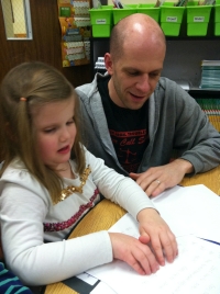 Photo of child reading braille with her father