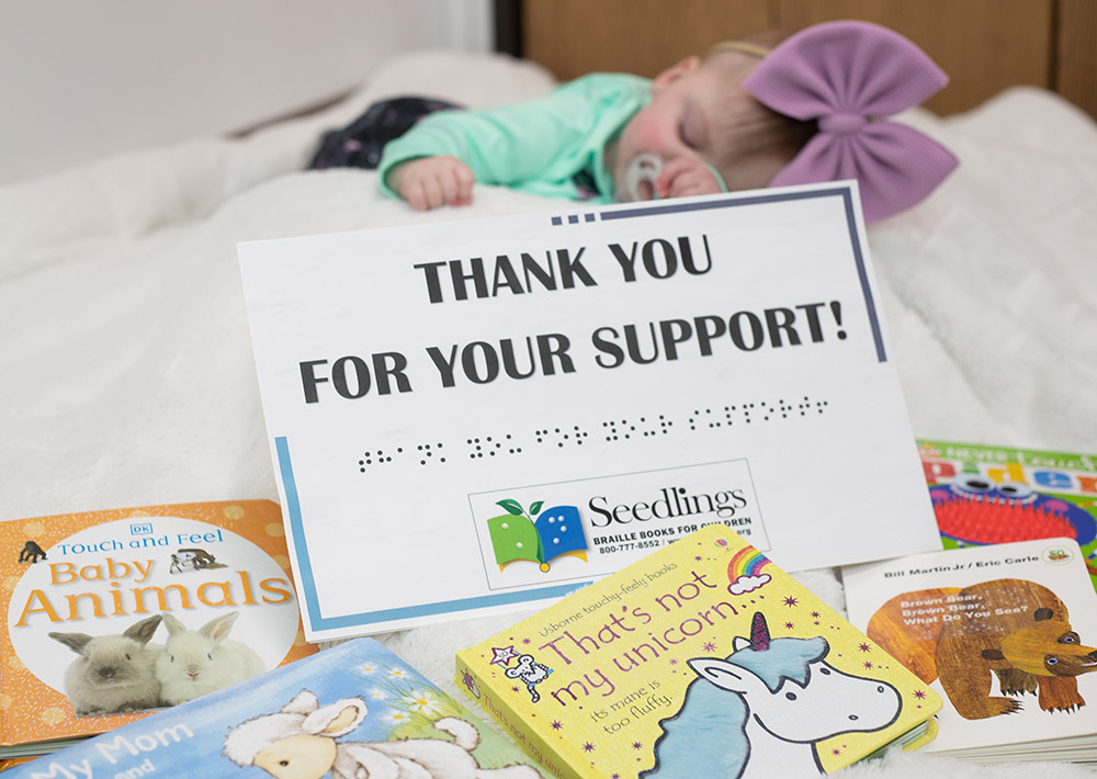 Thank you for your support Photograph of a baby with braille books an Thank You for Your Support sign