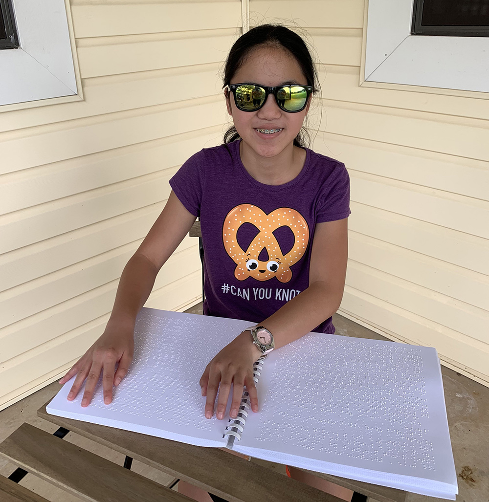 Emma-Securities Girl smiling while touching the pages of a braille-only book