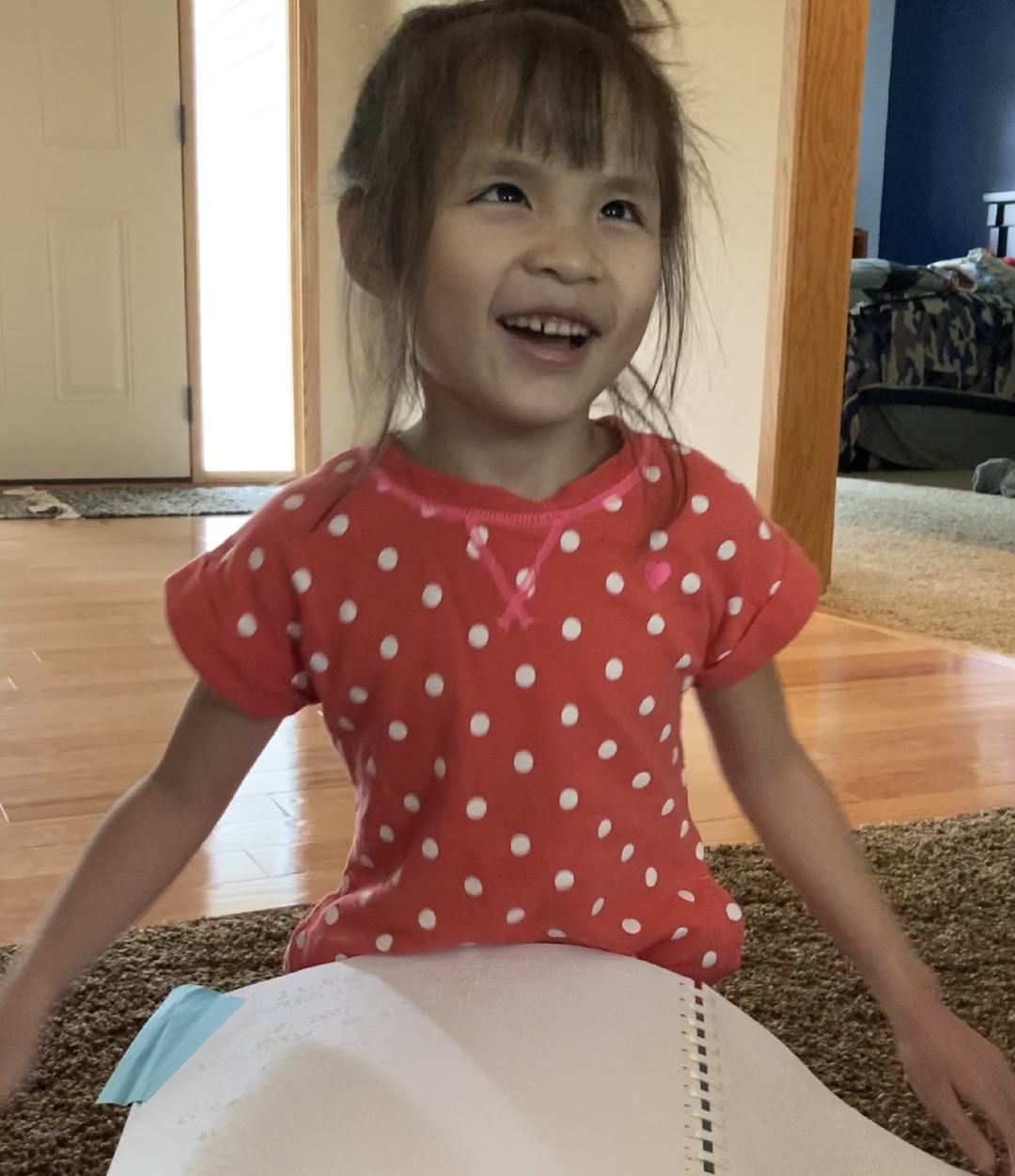 Winnie-Szymanski-crop A young girl sitting on the floor and smiling with a braille book