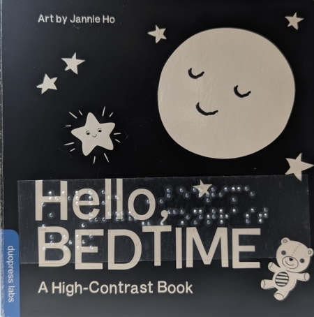 Cover of Hello, Bedtime with a black background and white print words, braille, and images of a moon, stars, and teddy bear